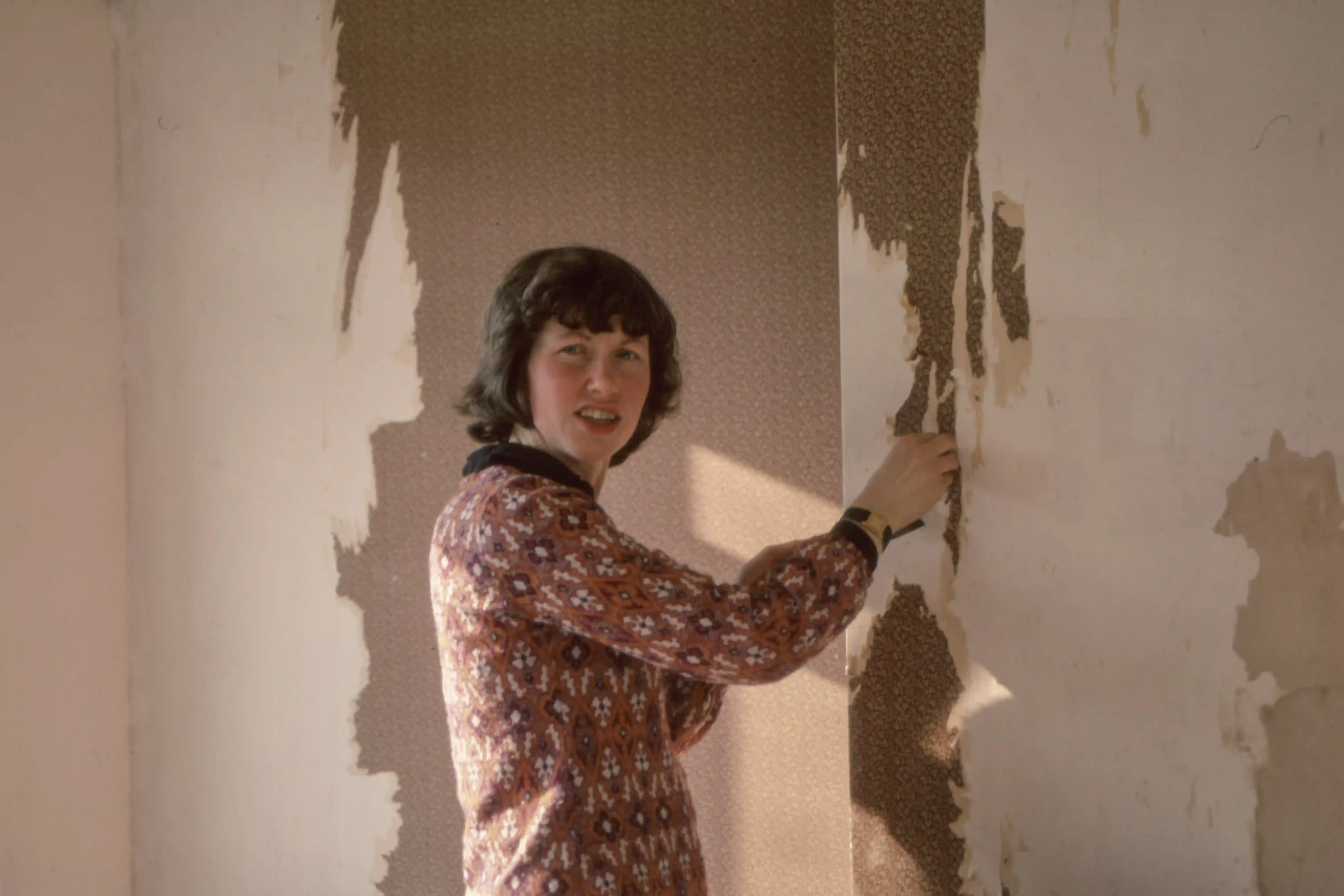 

A picture of a person wearing a tool belt and hard hat, standing in a newly renovated room with fresh paint and new furniture.